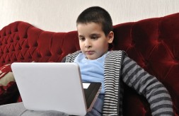 Child sitting on couch looking at laptop on lap.