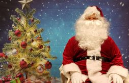 Santa Claus poses in front of a Christmas tree backdrop at the DSCC Mokena Regional Office.