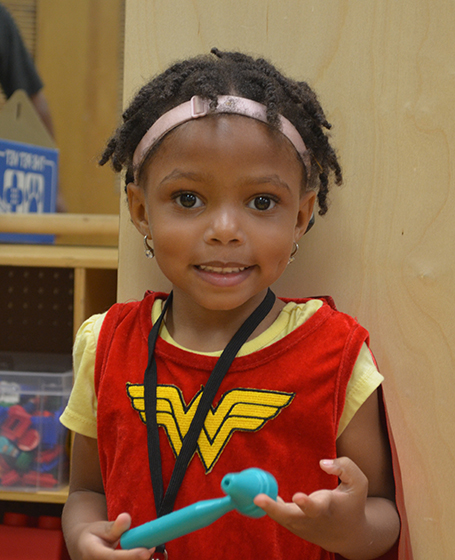 Little girl with hearing aids smiling while wearing a Wonder Woman costume