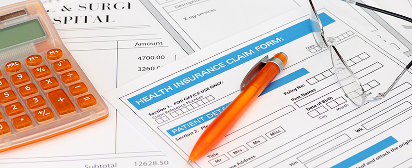 stack of health insurance forms with pen, calculator and pair of reading glasses