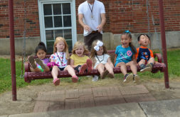 Six young children with hearing loss laugh as they sit on a swing together