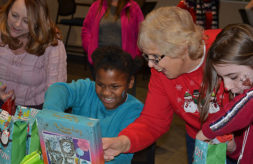 A Club Compass student smiles as she opens a Christmas present donated by Division of Specialized Care for Children Staff