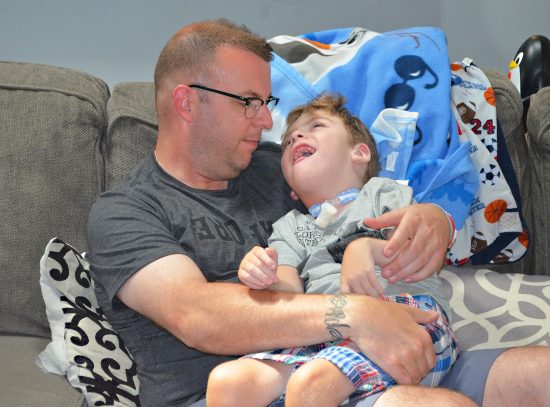 A medically complex little boy smiles up at his father while sitting in his arms