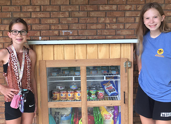 Emma Wiker and her sister, Ellen, stand on either side of a community pet pantry they opened in Athens, Ill.